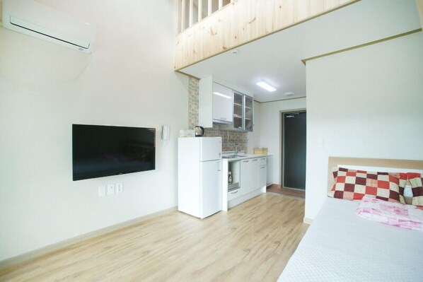 A compact room with a bed, a TV mounted on the wall, a small kitchenette, and a wooden ceiling. - Olleh House (Seogwipo)