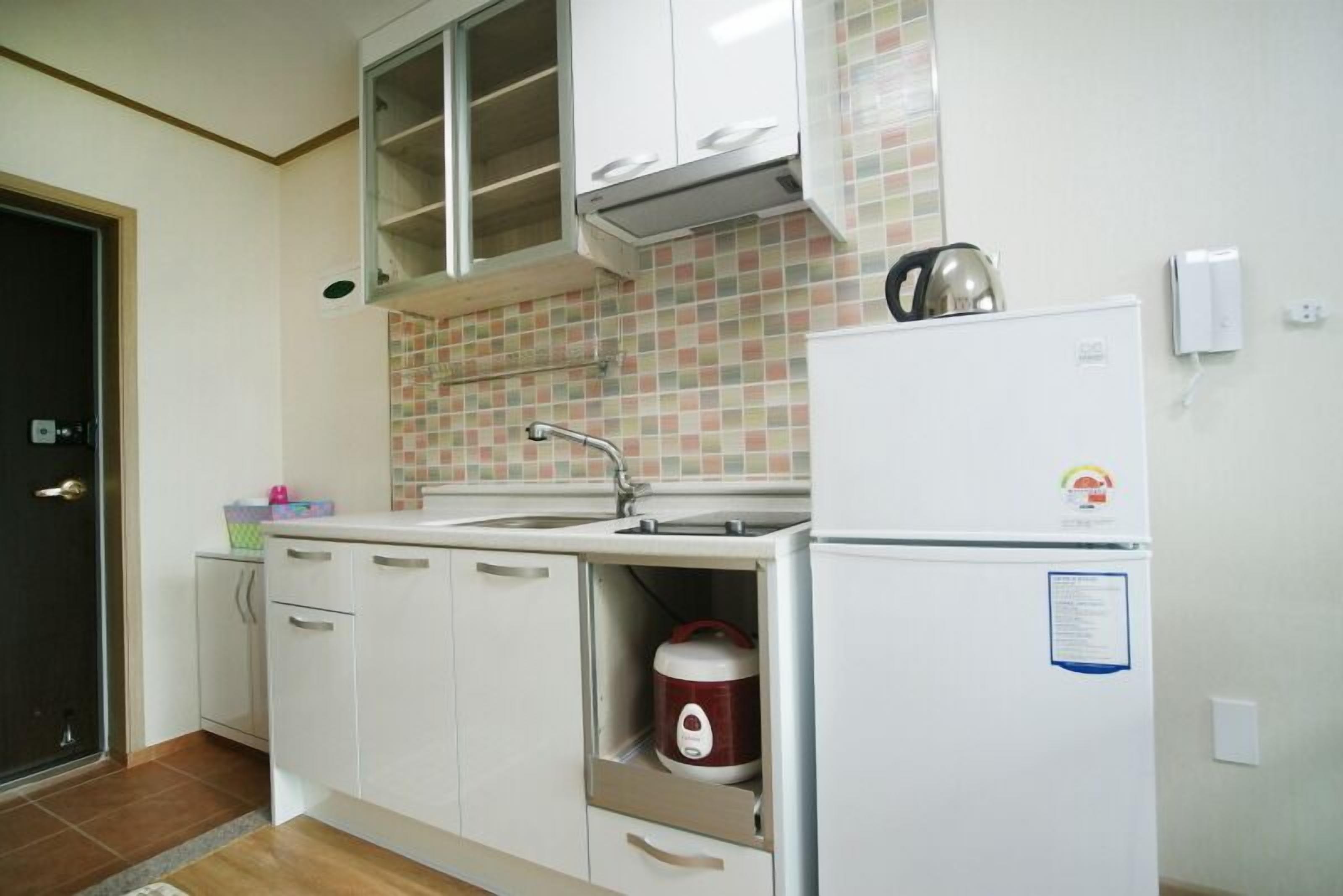 A compact kitchen with white cabinets, a built-in sink, and a refrigerator.