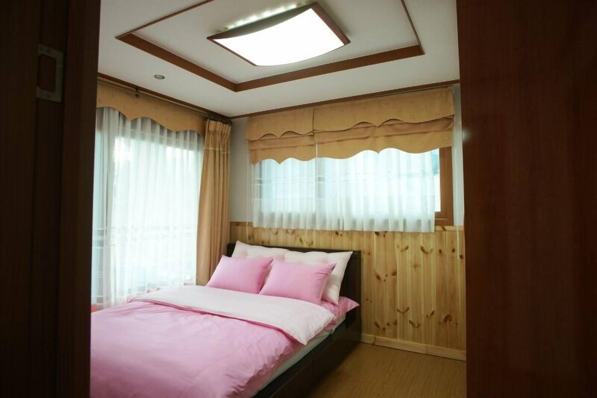 A bedroom with a bed, wooden paneling, a ceiling light, and curtains.