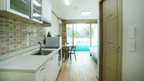 A compact kitchen with a sink, cabinets, and a dining area with a table and chair. - Olleh House (Seogwipo)
