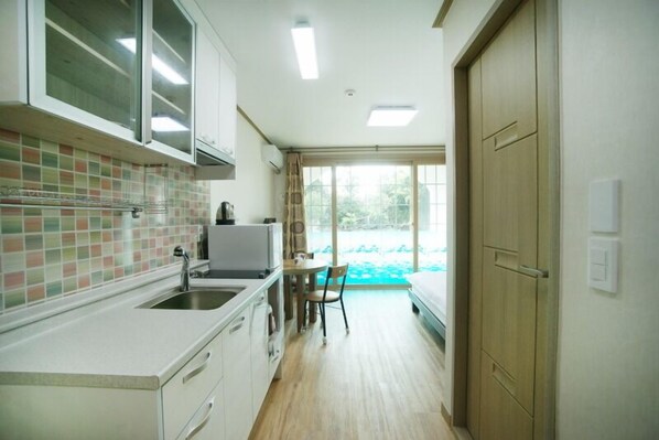 A compact kitchen with a sink, cabinets, and a dining area with a table and chair. - Olleh House (Seogwipo)