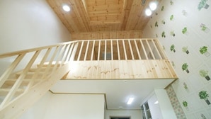 A wooden staircase leading to an upper floor with a kitchen area below. - Olleh House (Seogwipo)