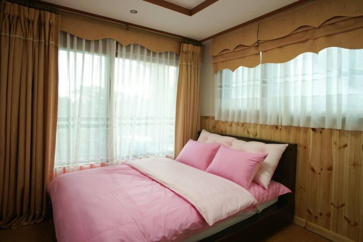 A bedroom with a bed, curtains, and wooden paneling.