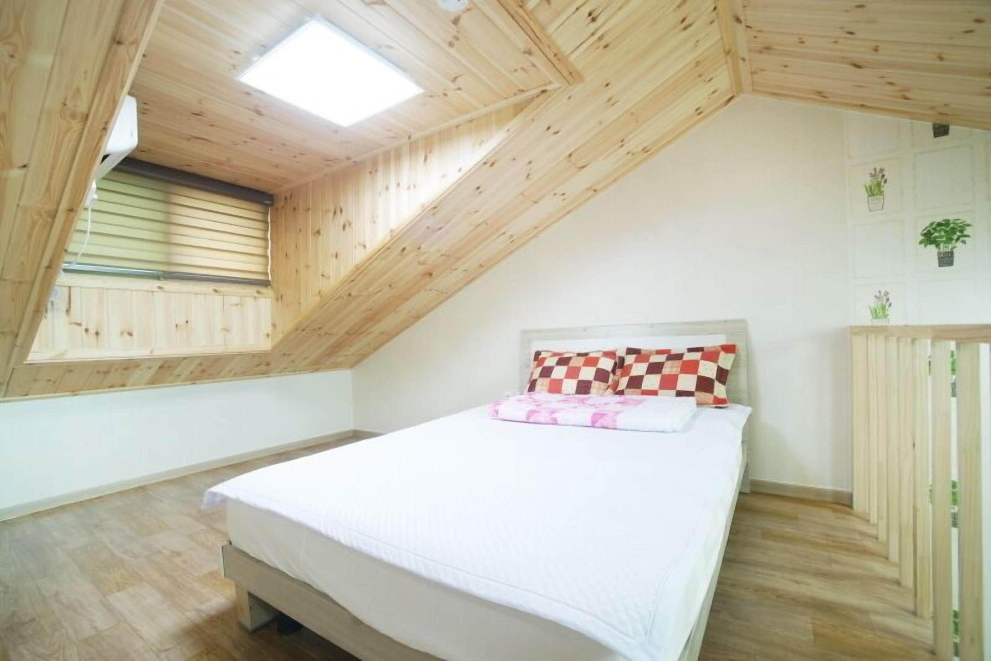 A bedroom with a sloped ceiling, a bed with a checkered pillow, and a small window.
