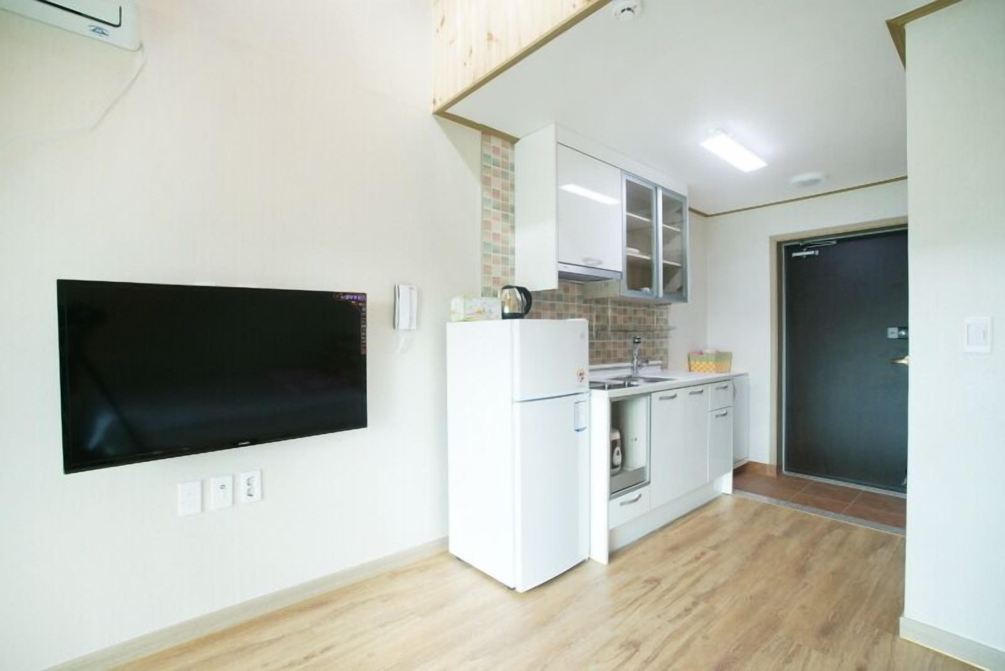 A compact kitchen with white cabinetry, a built-in oven, and a flat-screen TV mounted on the wall.