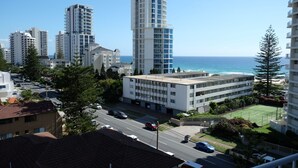 A high-rise building with a view of the ocean, surrounded by other buildings and a road with cars.