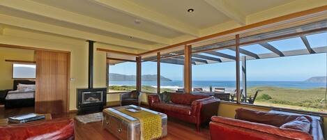 A spacious living room with a large window overlooking a scenic ocean view, furnished with leather sofas and a vintage suitcase.