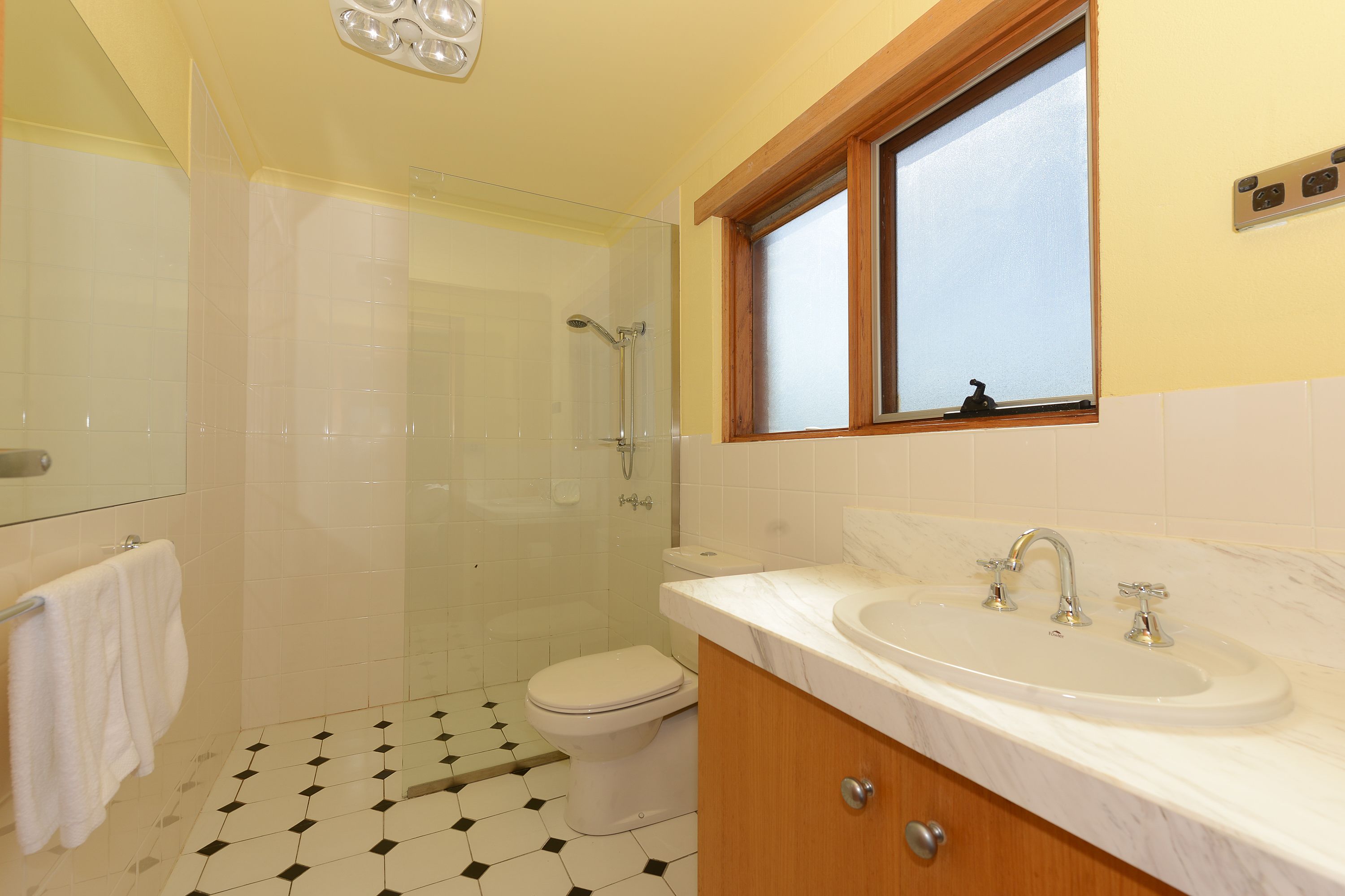 A bathroom with a shower, toilet, sink, and a window above the sink.