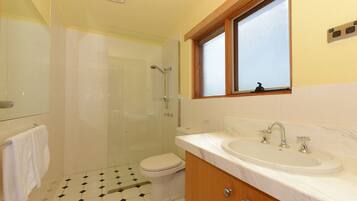 A bathroom with a shower, toilet, sink, and a window above the sink.