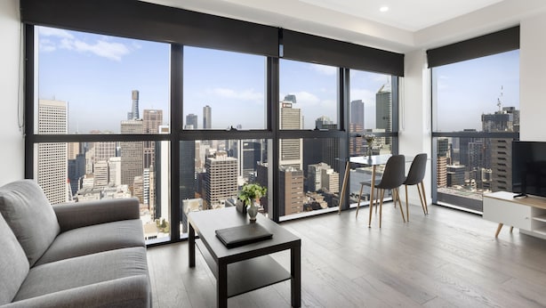 Una sala de estar moderna con ventanas amplias, un sofá, una mesa de centro y un televisor.
