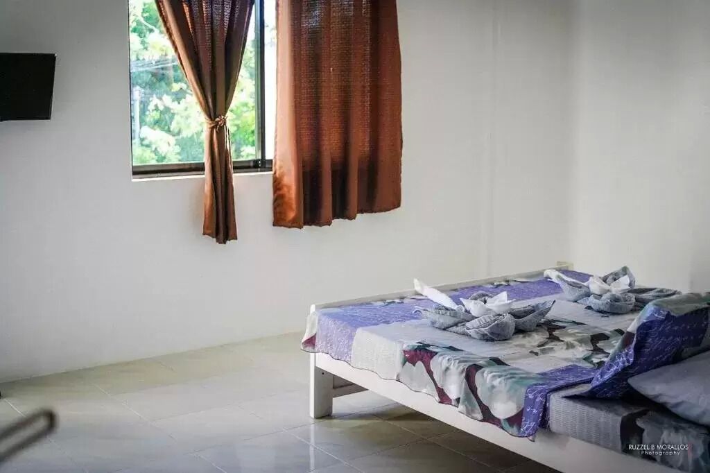 A simple room with a bed, a window with curtains, and a wall-mounted TV.