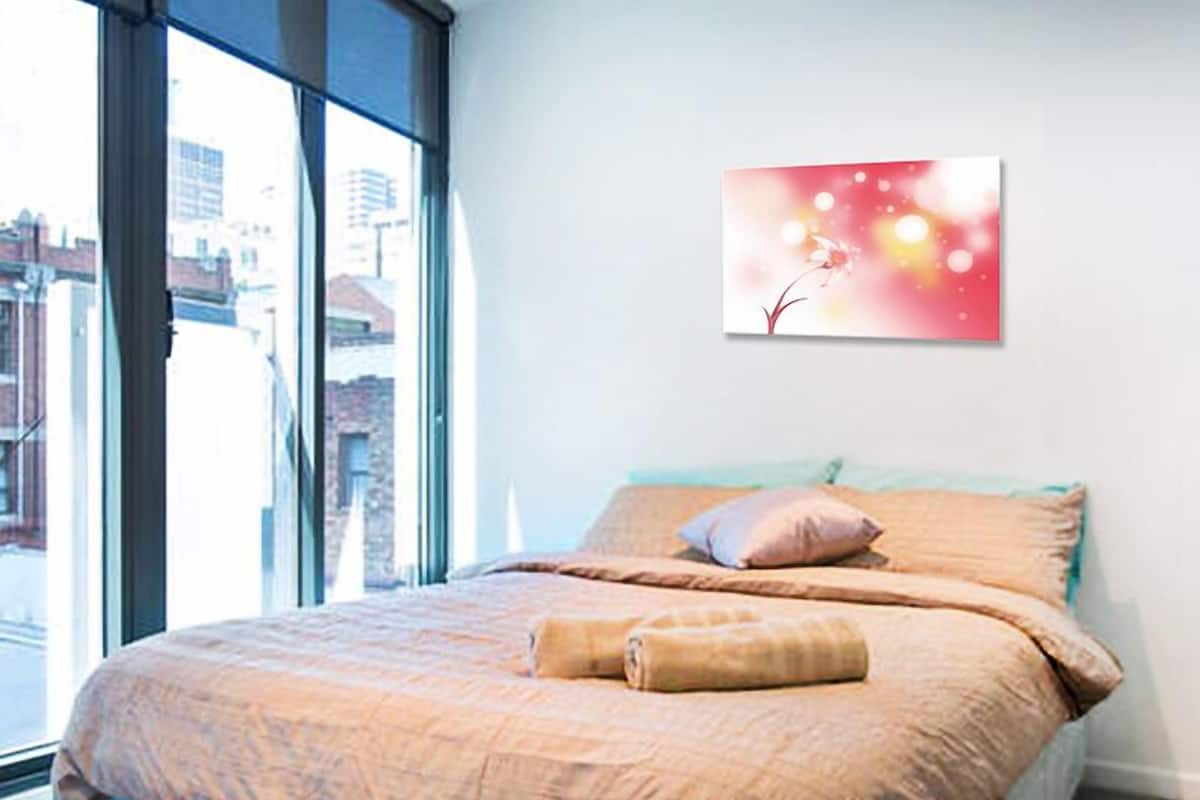 A bedroom with a large window, a bed with beige bedding, and a wall-mounted picture.