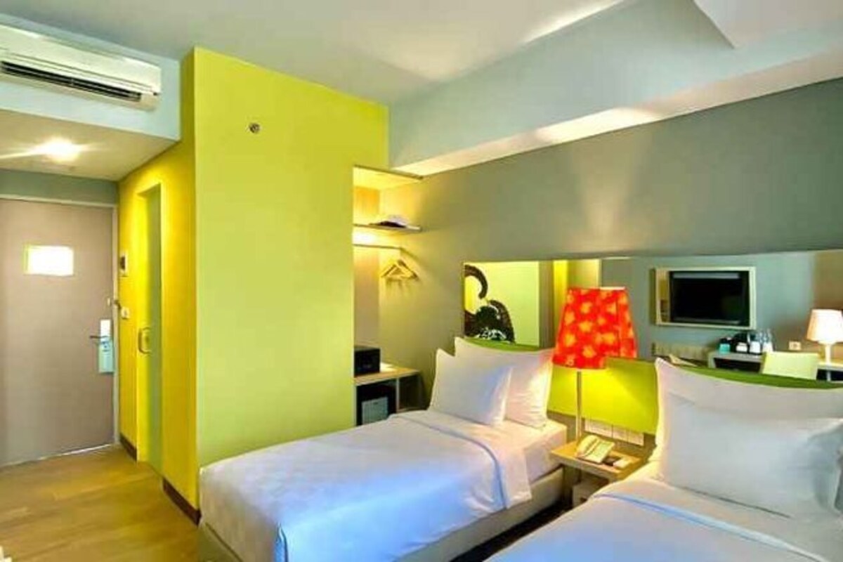 Una habitación de hotel con cama, mesita de noche, lámpara y televisor.