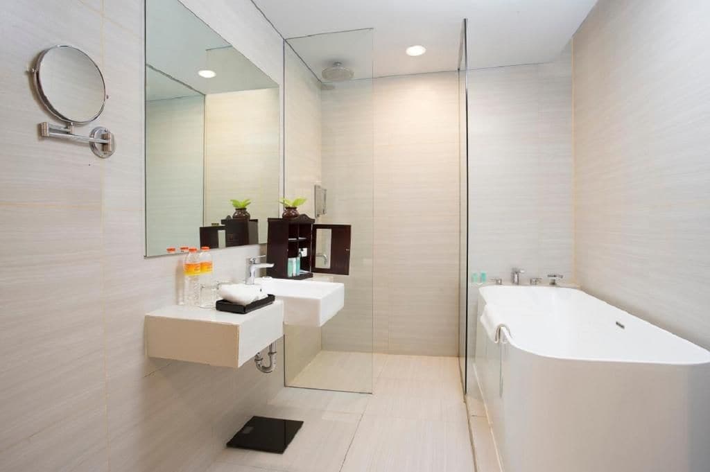 Un baño moderno con cabina de ducha de vidrio, dos lavamanos, una bañera grande y un espejo con marco redondo.