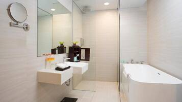 Un baño moderno con cabina de ducha de vidrio, dos lavamanos, una bañera grande y un espejo con marco redondo.