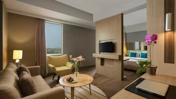 Habitació d'hotel amb sofà, butaca, taula de centre, televisió i llit amb vistes.