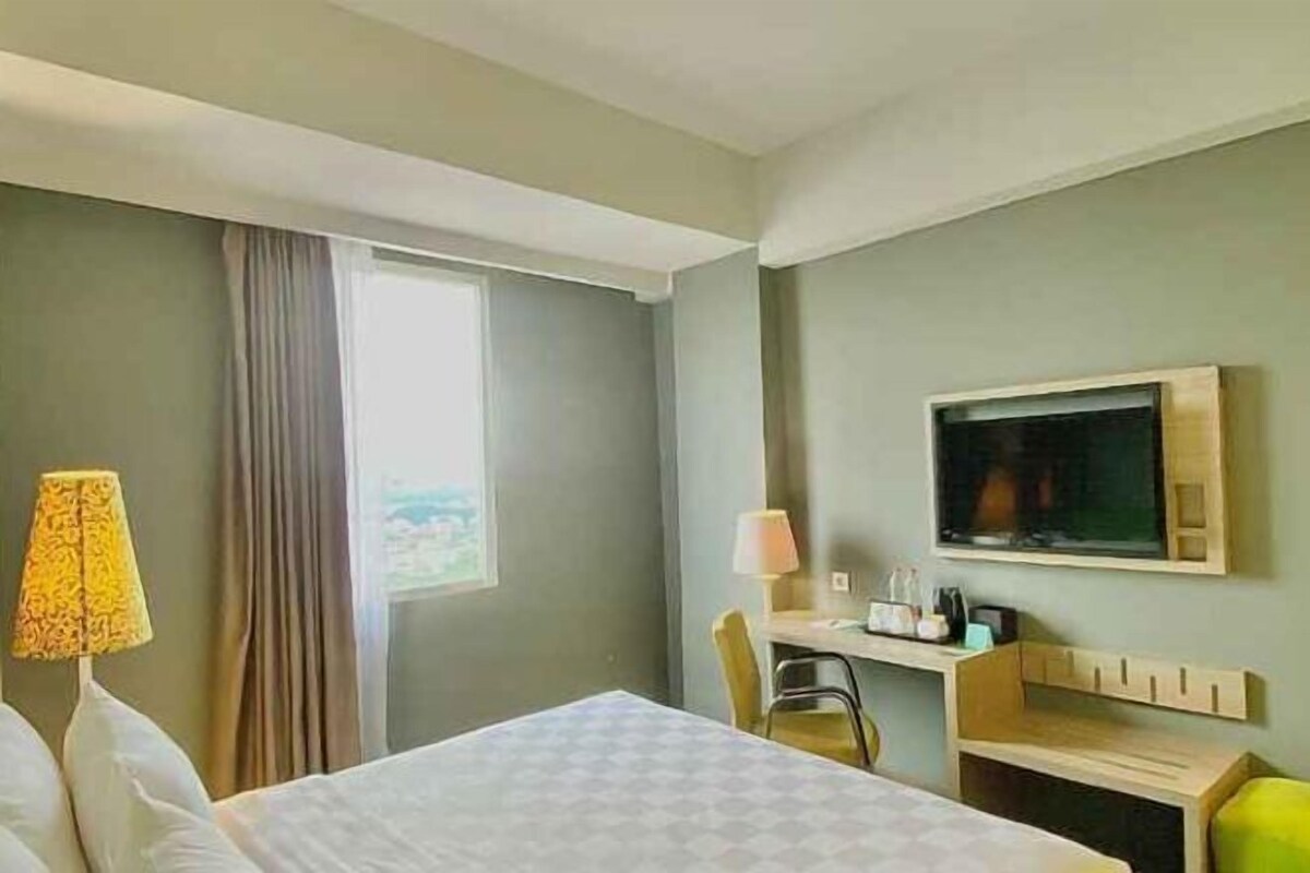 A hotel room with a bed, a desk, a chair, a television, and a window with curtains.