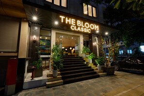 L’entrée d’un hôtel, avec une enseigne indiquant « THE BLOOM CLASSIC », des marches menant à l’entrée et des plantes en pot.