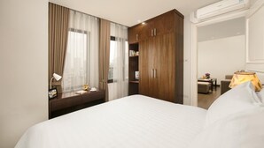 Un dormitorio de hotel con una cama grande, un armario de madera, un escritorio con lámpara y vistas a la ciudad a través de la ventana.