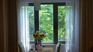 Una mesa de comedor servida con una botella, copas, platos y un jarrón de girasoles junto a una ventana con vistas a follaje exuberante.