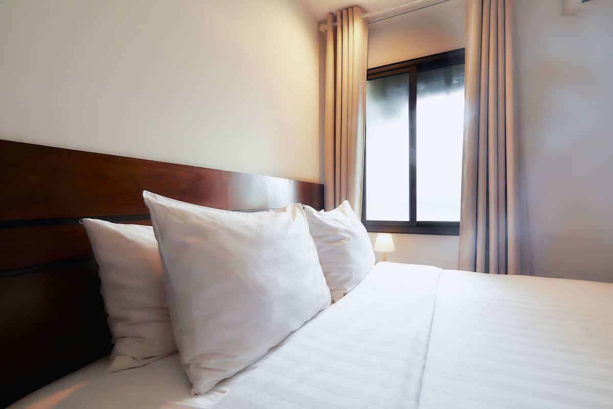 Habitación de hotel con cabecera de madera, ropa de cama blanca y ventana con cortinas.