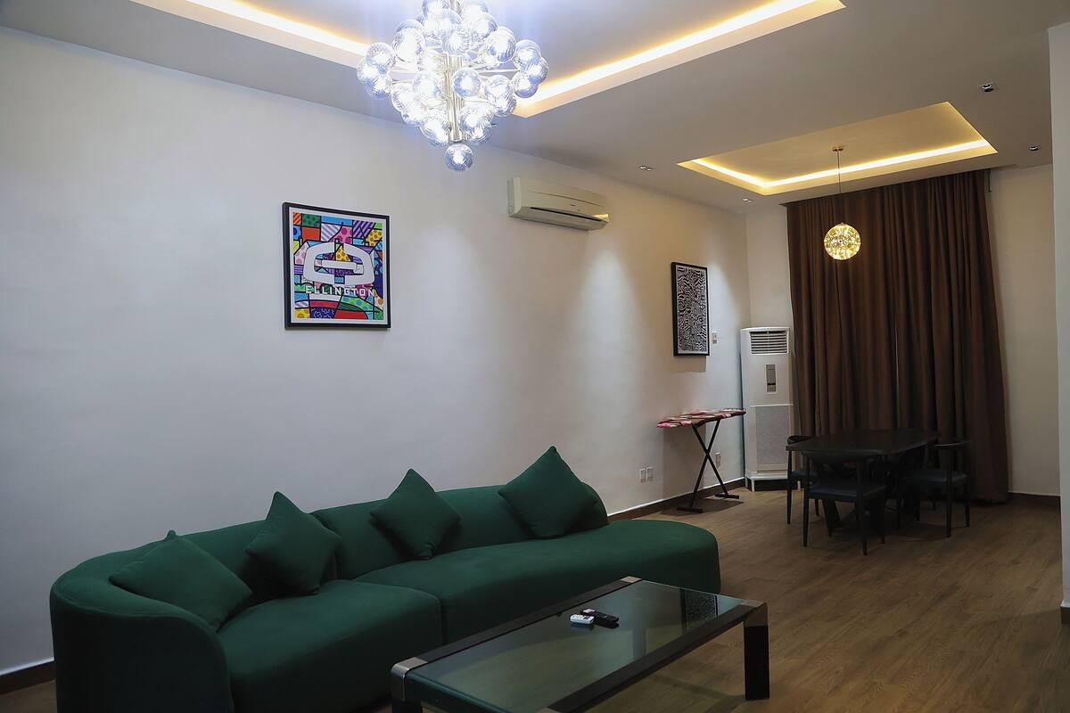 A modern living room with a green sofa, a glass coffee table, and a dining area with a table and chairs.