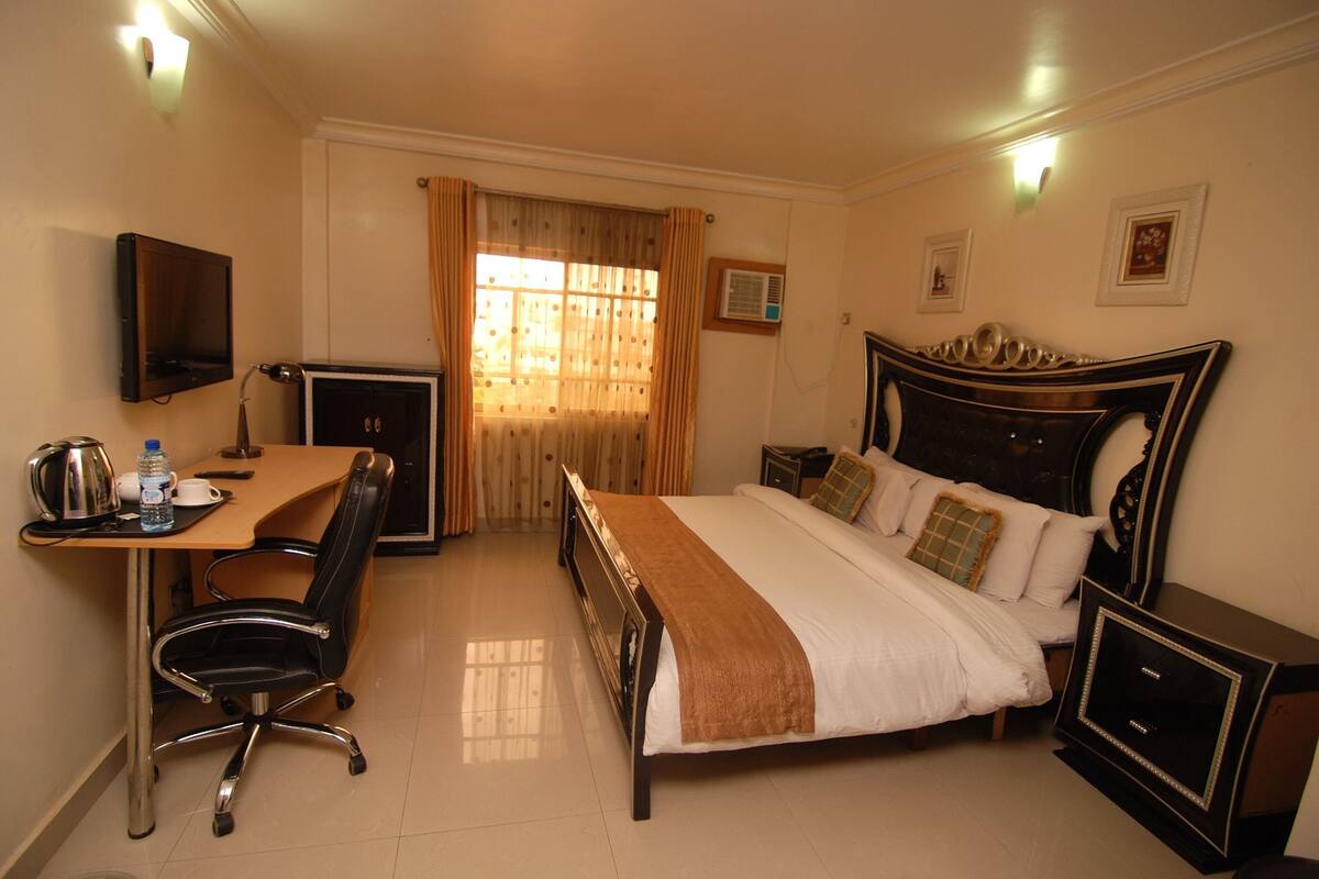 Habitación de hotel con cama, escritorio con silla, televisión y ventana con cortinas.