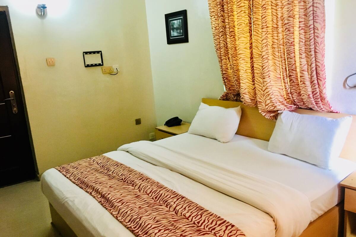 Ein Hotelzimmer mit einem Bett, einem Nachttisch, einem Telefon und einem an der Wand montierten Lichtschalter.