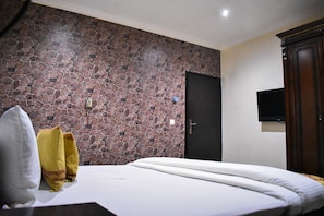 A bedroom with a stone-patterned wall, a bed with white bedding, a wooden wardrobe, and a flat-screen TV mounted on the wall. - Béni Apartments (Lagos)