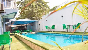 A swimming pool with green chairs and a table, surrounded by a white wall and a tree. - Béni Apartments (Lagos)
