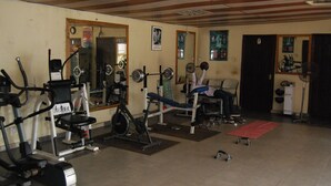 Ein Fitnessstudio mit unterschiedlichen Trainingsgeräten, darunter eine Langhantelbank, ein Squat-Gestell und ein Laufband.