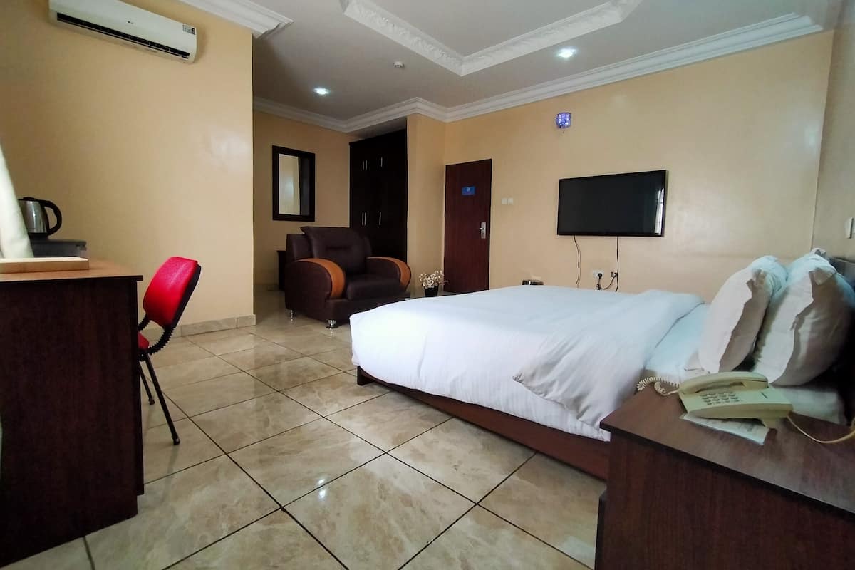 Habitación de hotel con cama, escritorio con teléfono, silla, equipo de aire acondicionado y televisor.
