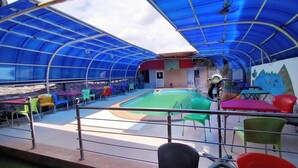 A covered outdoor area with a pool, seating, and a fan. - Laps New World Hotel (Abuja)
