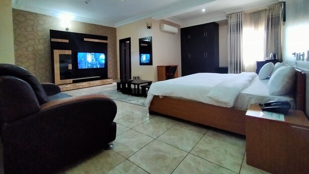 A hotel room with a large bed, a TV, a desk, and a seating area. - Laps New World Hotel (Abuja)
