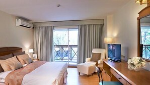 Een hotelkamer met een bed, een bureau met een televisie, een stoel, een bureaulamp en een raam met gordijnen.