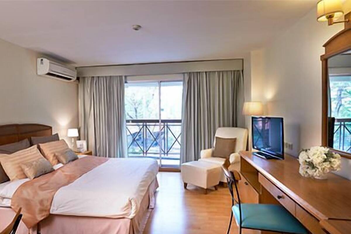 Habitación de hotel con cama, escritorio con televisor, silla, lámpara de escritorio y ventana con cortinas.
