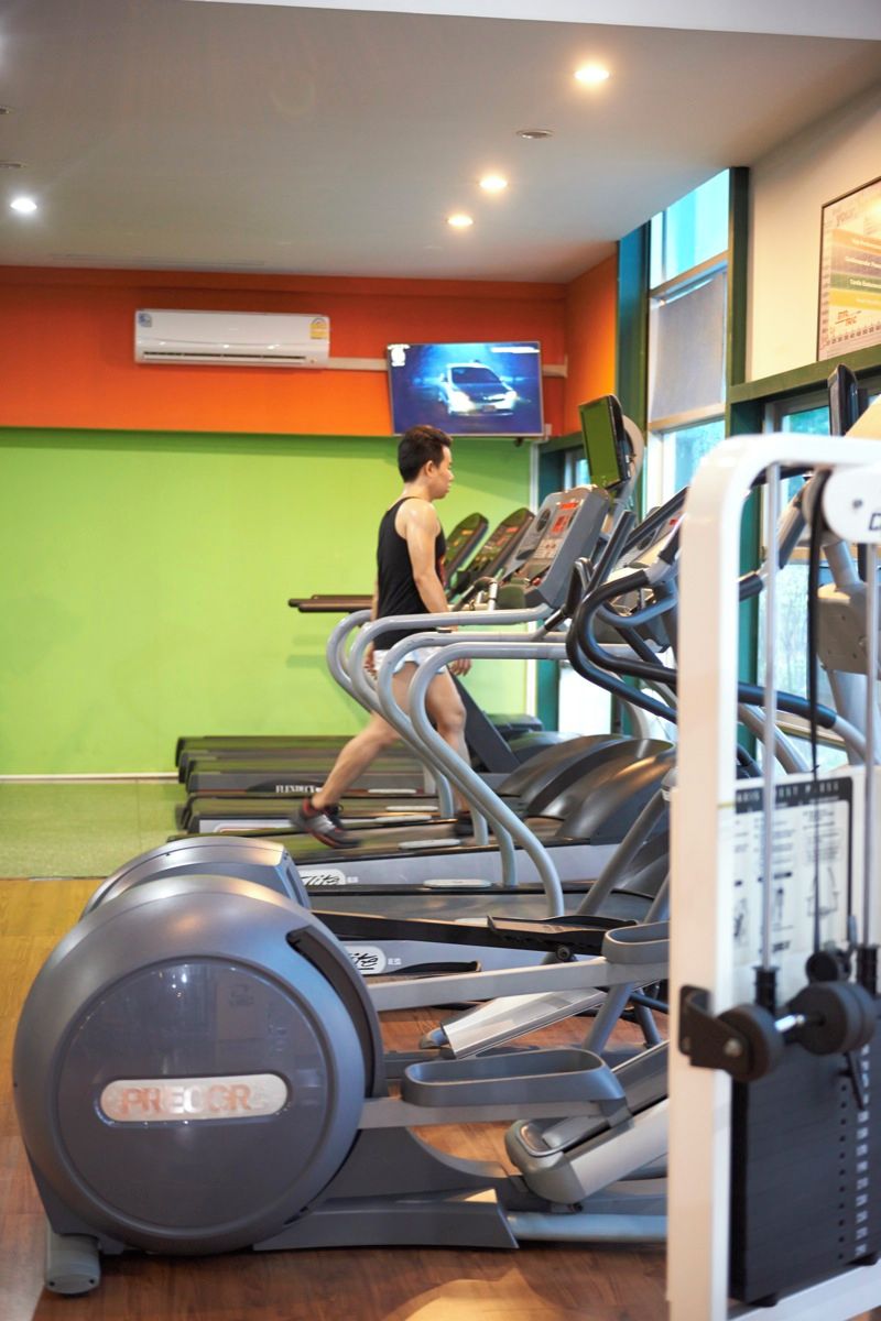 A gym with treadmills, a television on the wall, and a green wall.