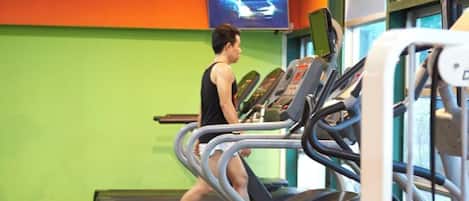 Un gimnasio con cintas de correr, un televisor en la pared y una pared verde.