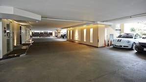Een overdekte parkeerplaats met betonnen vloer, een witte auto geparkeerd rechts en een gebouwdeur links.