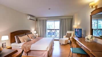 A hotel room with a bed, a desk, a chair, a television, and a balcony view.