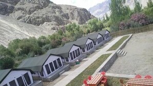 A row of cabins with large windows, a paved path, and outdoor seating with tables and chairs. - Nubra Summer Camp (Leh)