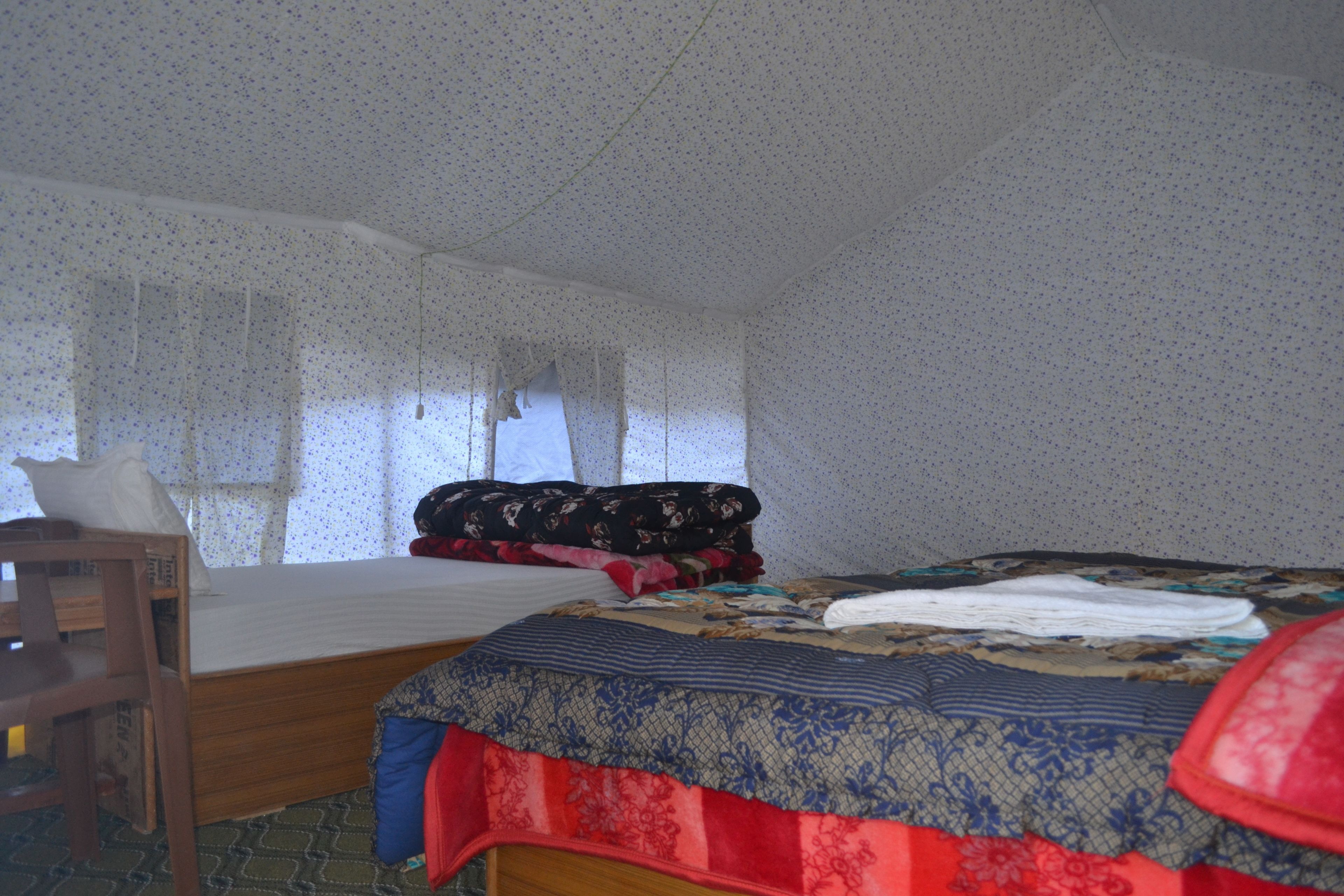 A room with a bed, a wooden chair, and a window with curtains.
