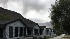 A row of identical tents with a number on the front, set against a mountainous backdrop. - Nubra Summer Camp (Leh)