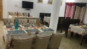 A dining area with multiple tables and chairs, a television mounted on the wall, and framed pictures on the wall. - Nubra Summer Camp (Leh)