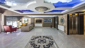 A spacious lobby with a modern chandelier, a fireplace, a large TV, and a patterned floor. - Madi Otel Izmir (Izmir)