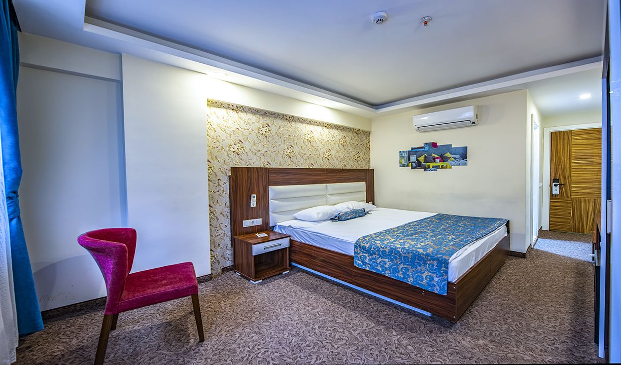 A hotel room with a bed, a nightstand, a red chair, and a patterned carpet.