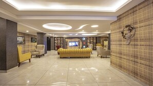 A spacious lobby with a yellow sofa, multiple armchairs, and a television. - Madi Otel Izmir (Izmir)