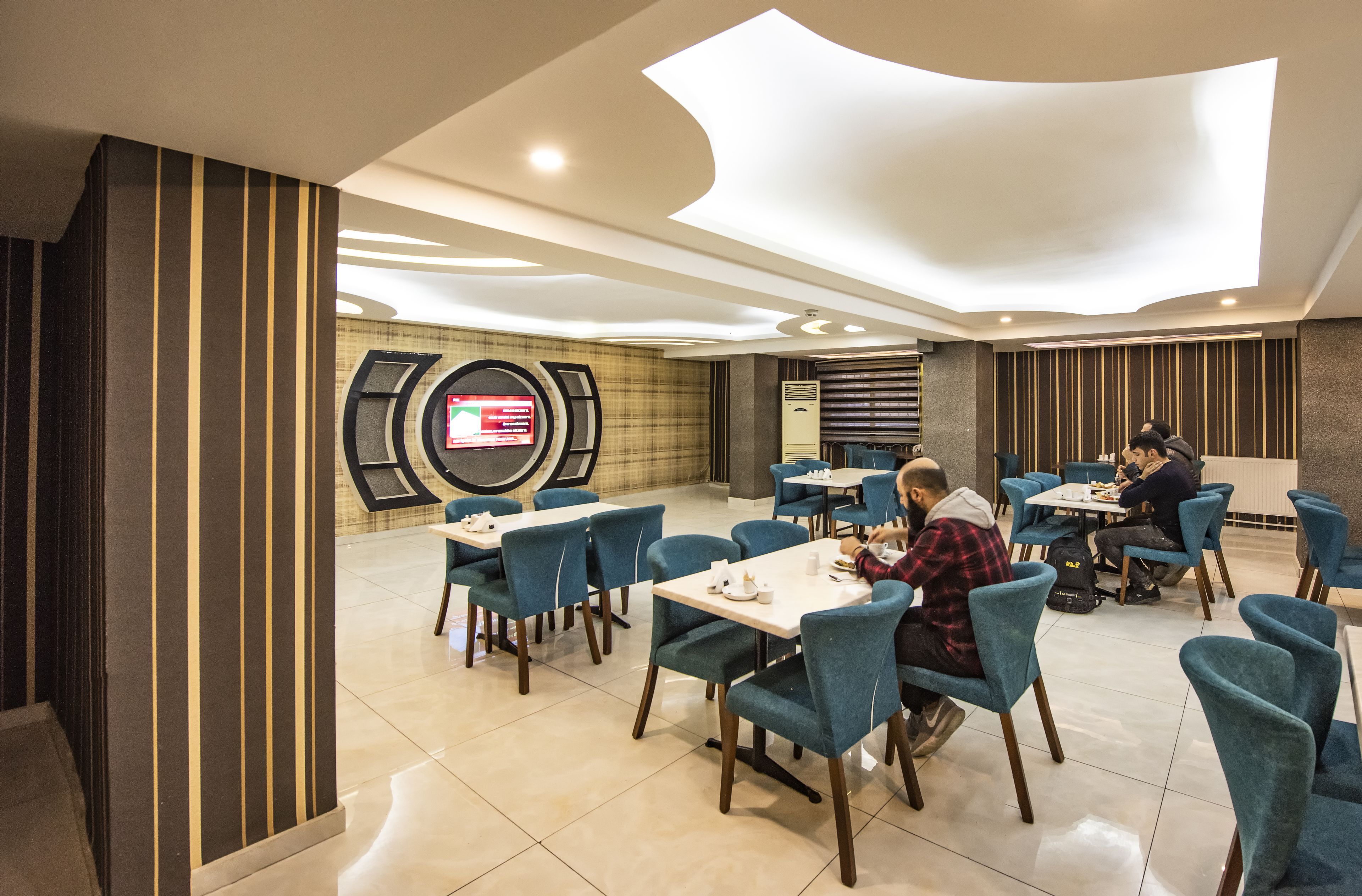 A modern dining area with blue chairs and tables, a large screen displaying a menu, and a contemporary ceiling design.