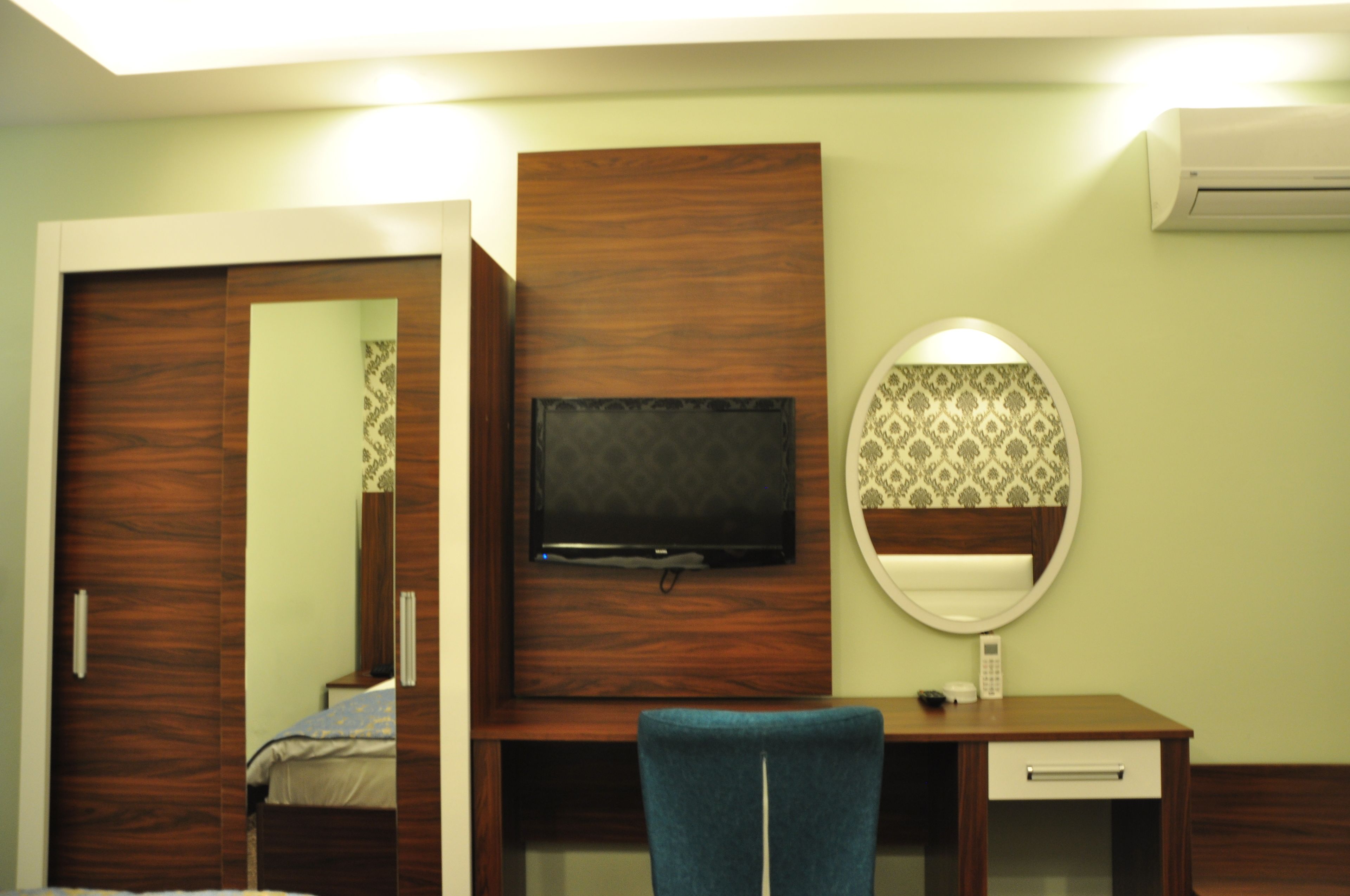 Une chambre à coucher comprenant une armoire en bois, un lit, un bureau avec une chaise, une télévision et un miroir.