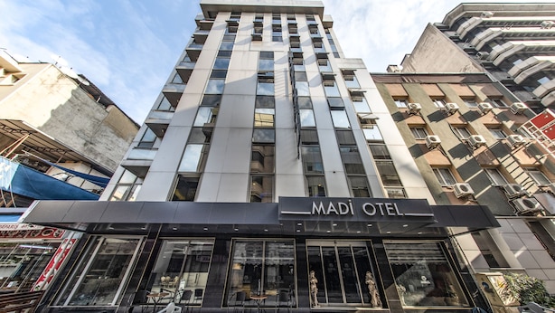 A modern hotel with a prominent sign reading "MADI OTEL". It features a large entrance with glass doors and a seating area outside. - Madi Otel Izmir (Izmir)